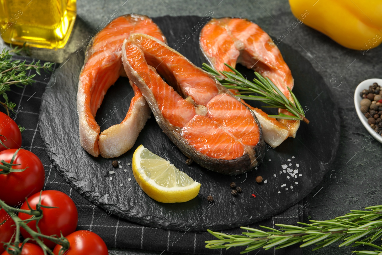 Photo of Tasty grilled salmon steaks, tomatoes, oil and spices on gray textured table, closeup