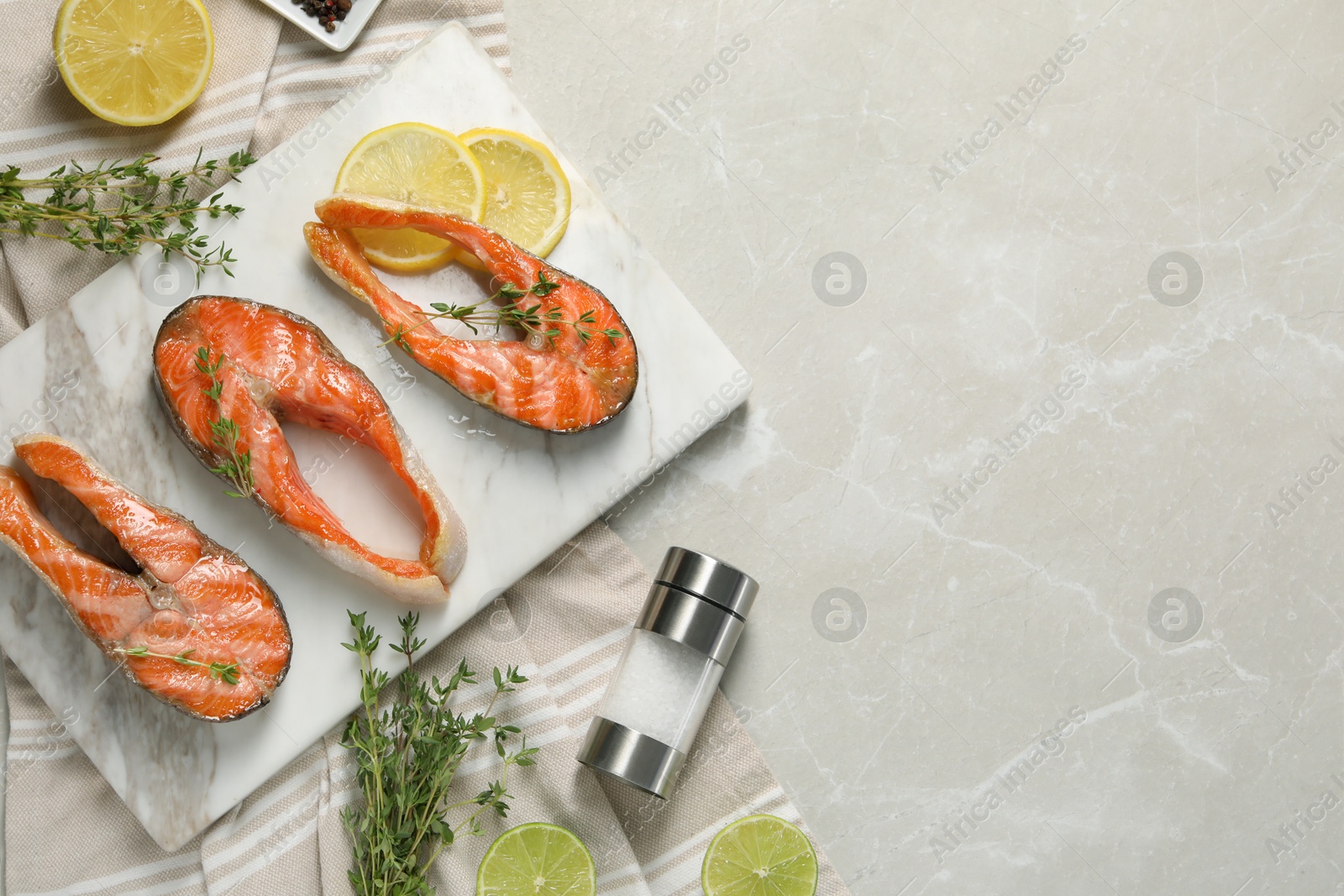 Photo of Tasty grilled salmon steaks, lemon, lime and spices on gray marble table, flat lay. Space for text