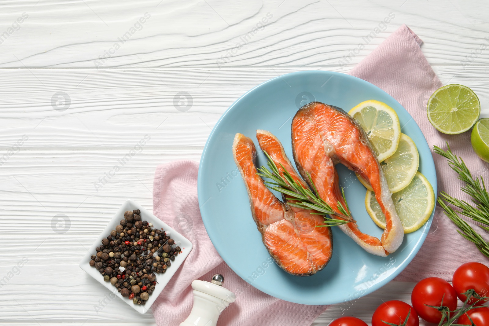 Photo of Tasty grilled salmon steaks, tomatoes, lemon, lime and spices on white wooden table, flat lay. Space for text