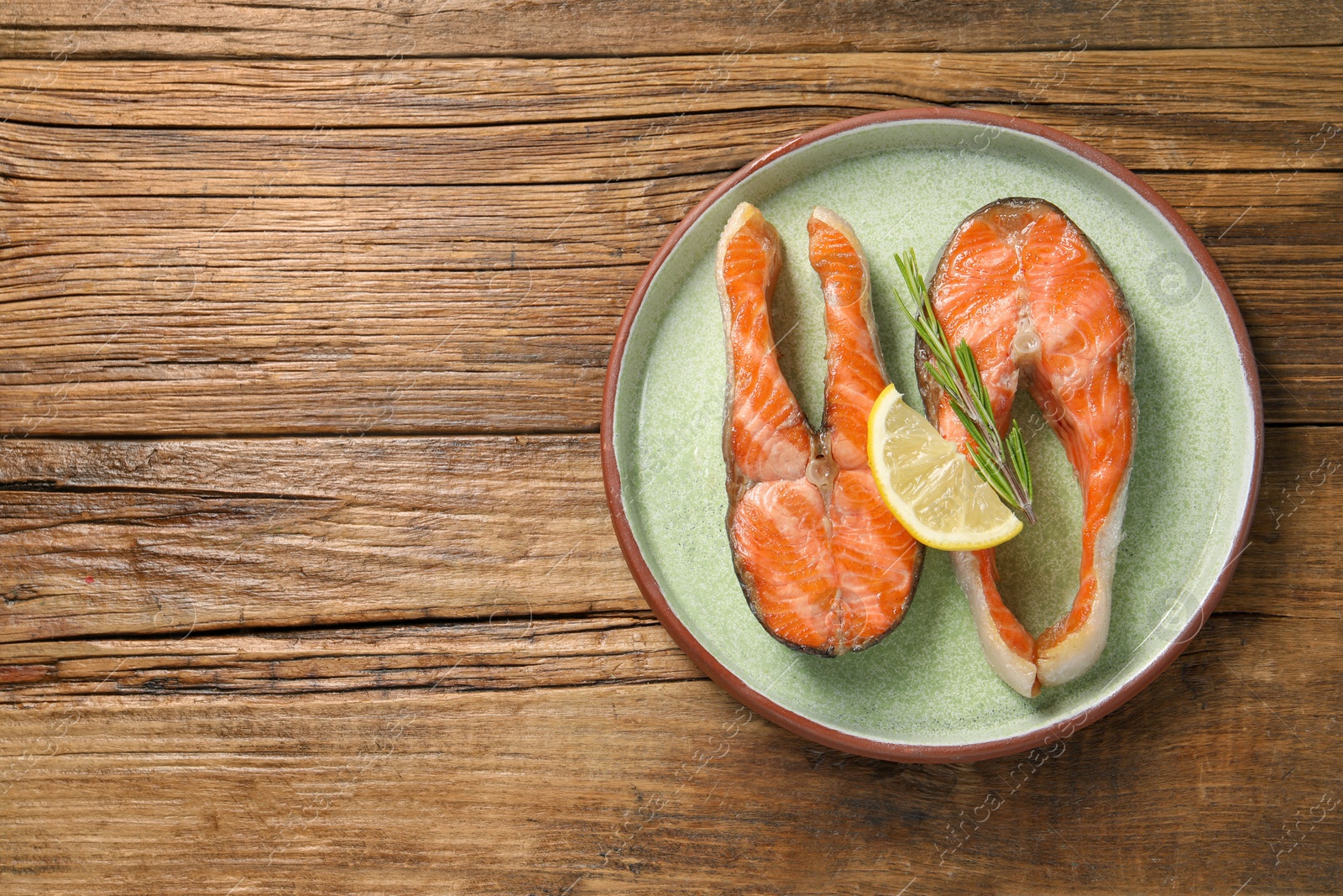 Photo of Tasty grilled salmon steaks, lemon and rosemary on wooden table, top view. Space for text