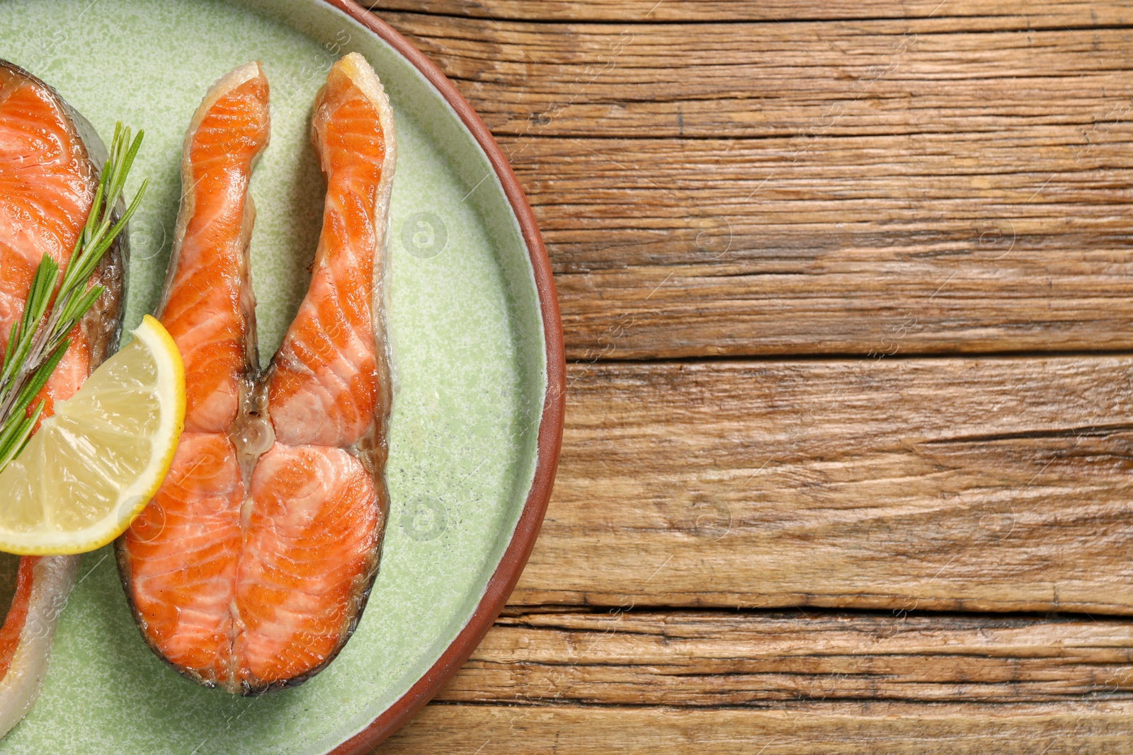 Photo of Tasty grilled salmon steaks, lemon and rosemary on wooden table, top view. Space for text