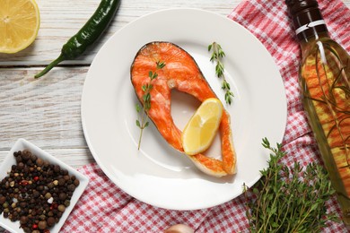 Tasty grilled salmon steak, oil, lemon and spices on wooden table, flat lay