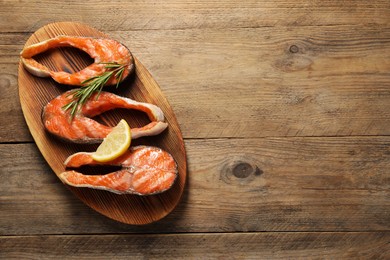 Photo of Tasty grilled salmon steaks, lemon and rosemary on wooden table, top view. Space for text