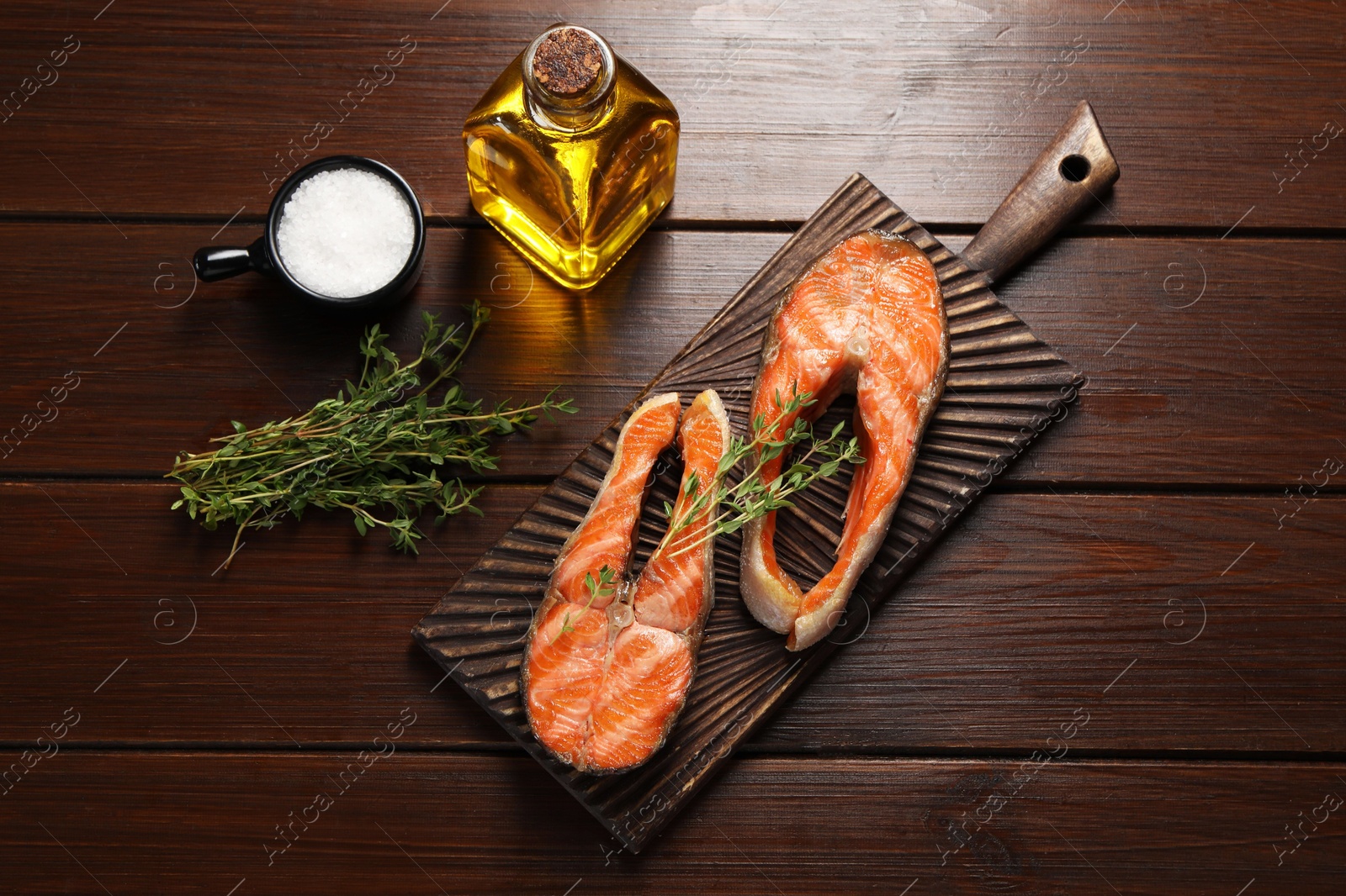 Photo of Tasty grilled salmon steaks, oil and spices on wooden table, flat lay