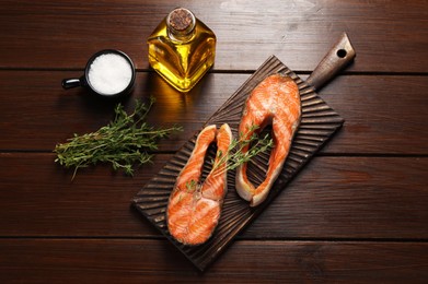 Photo of Tasty grilled salmon steaks, oil and spices on wooden table, flat lay