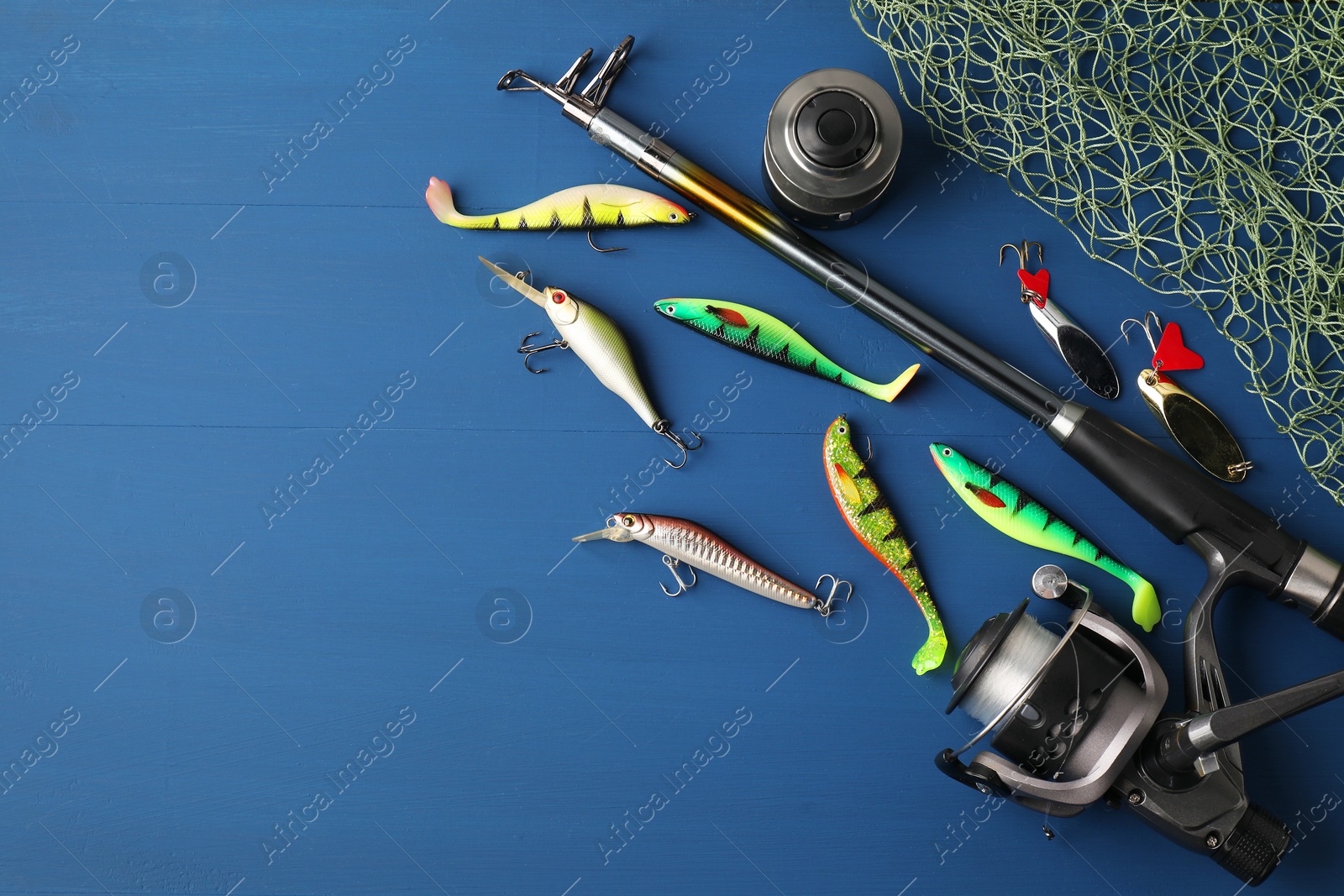 Photo of Fishing rod with spinning reel, baits and net on blue wooden table, flat lay. Space for text