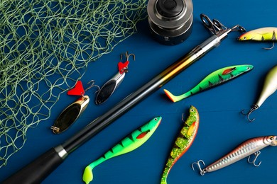 Photo of Fishing rod with spinning reel, baits and net on blue wooden table, flat lay