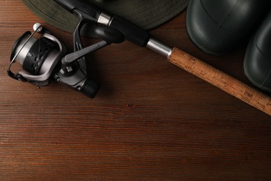 Fishing rod with spinning reel, hat and boots on wooden table, top view. Space for text