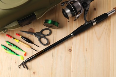 Fishing rod with spinning reel, baits, scissors, line and tackle box on wooden table, top view. Space for text