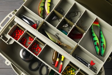 Different fishing tackles in box on grey wooden table, top view