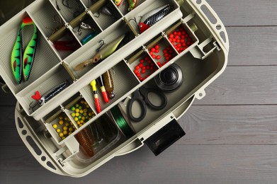 Different fishing tackles in box on grey wooden table, top view