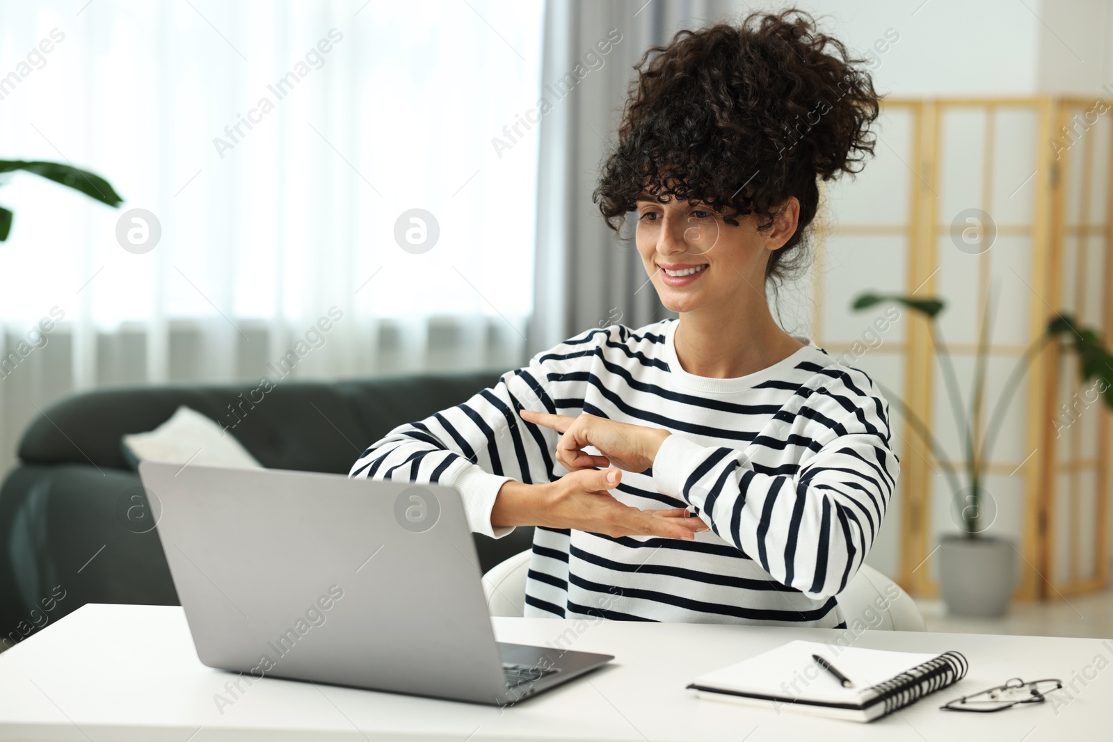 Photo of Young woman using sign language for communication during video call at white table indoors