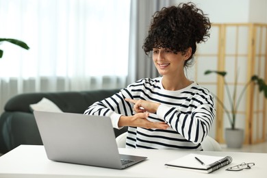 Young woman using sign language for communication during video call at white table indoors