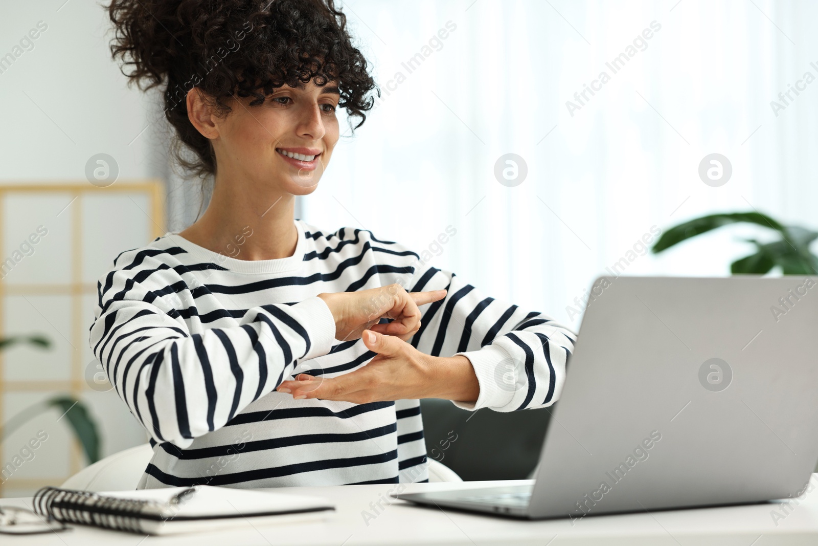 Photo of Young woman using sign language for communication during video call at white table indoors