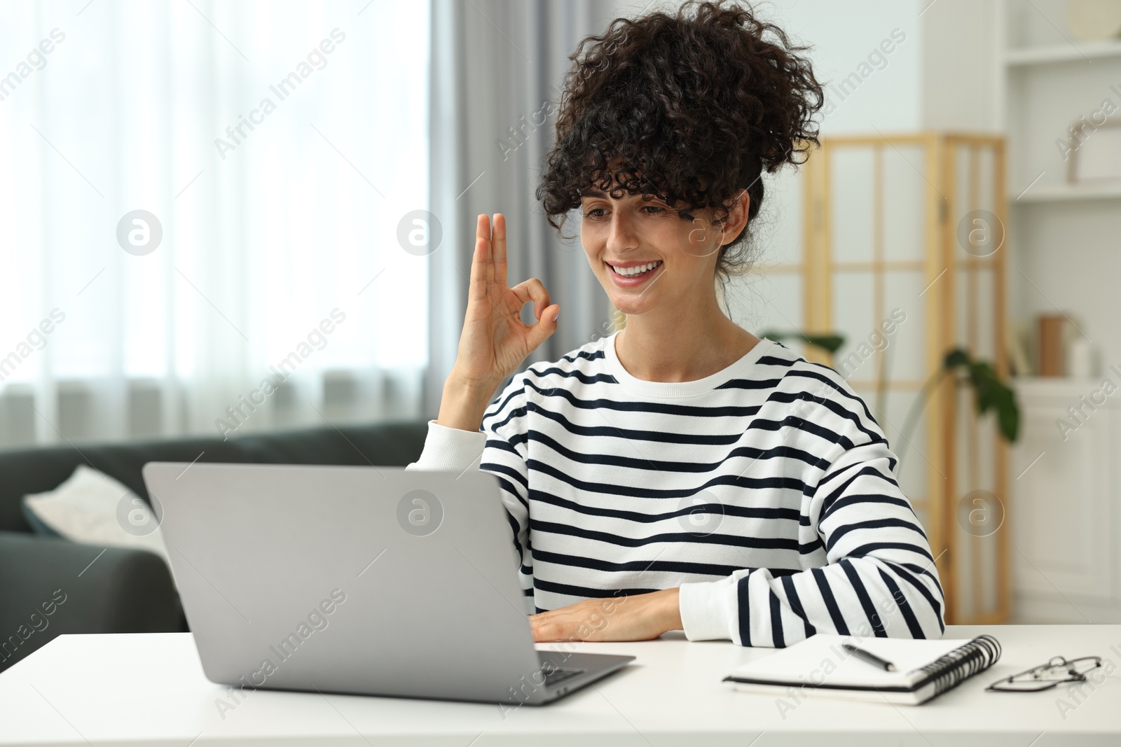 Photo of Young woman using sign language for communication during video call at white table indoors