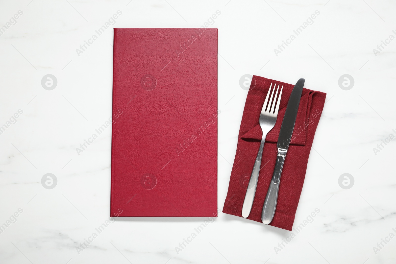 Photo of Hardcover menu and cutlery on white marble table, flat lay