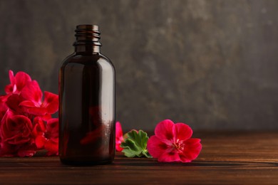 Photo of Geranium essential oil in bottle and beautiful flowers on wooden table