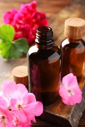 Photo of Geranium essential oil in bottles and beautiful flowers on table