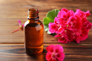 Photo of Geranium essential oil in bottle and beautiful flowers on wooden table