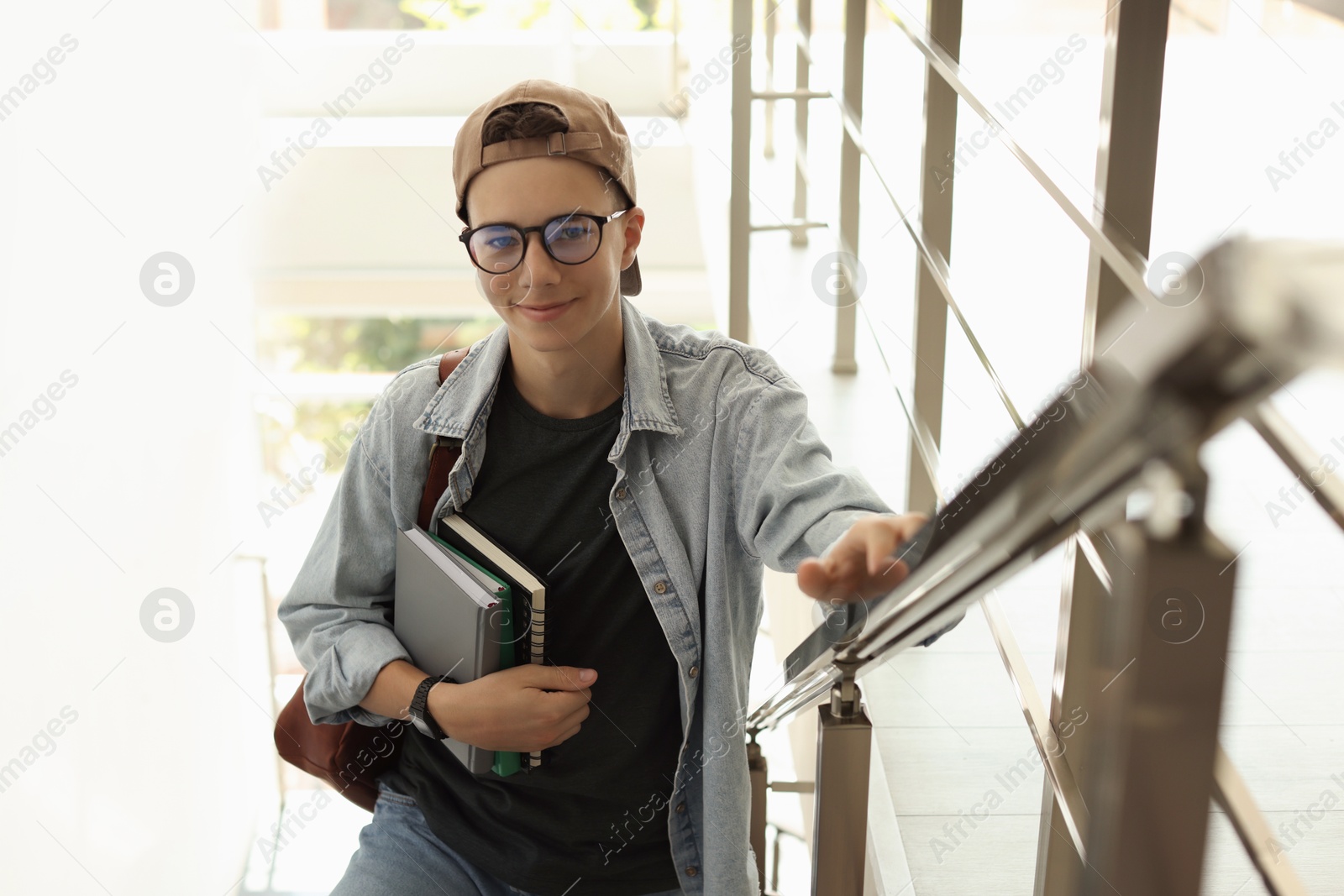 Photo of Portrait of teenage boy with books near railings indoors