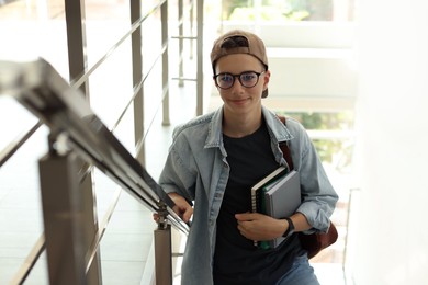 Photo of Portrait of teenage boy with books near railings indoors