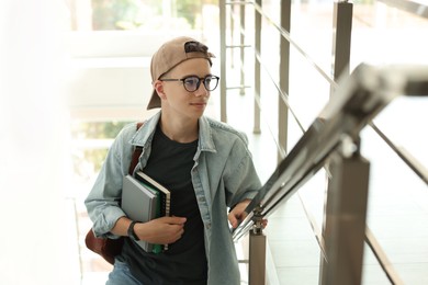 Photo of Portrait of teenage boy with books near railings indoors