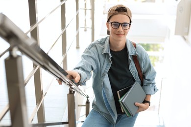 Photo of Portrait of teenage boy with books near railings indoors