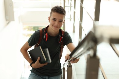 Photo of Portrait of teenage boy with books near railings indoors