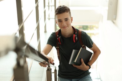 Photo of Portrait of teenage boy with books near railings indoors