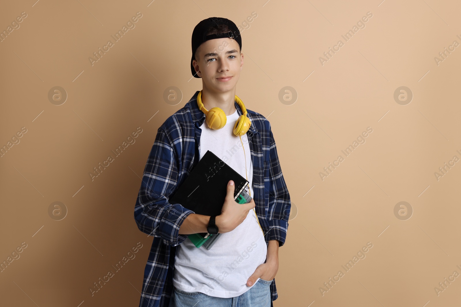 Photo of Portrait of teenage boy with books on dark beige background