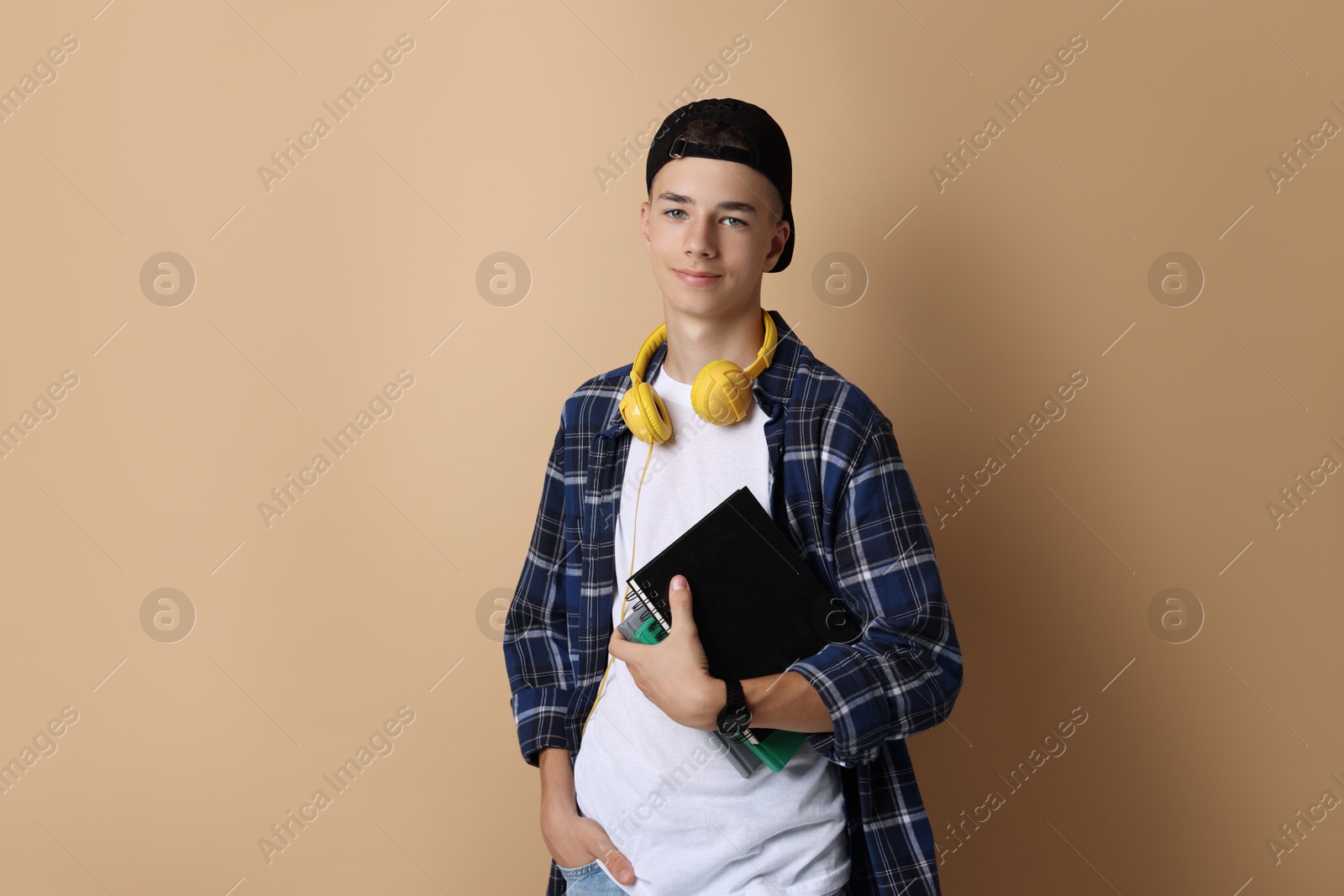 Photo of Portrait of teenage boy with books on dark beige background