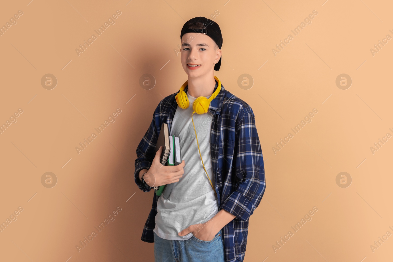 Photo of Portrait of smiling teenage boy with books on dark beige background