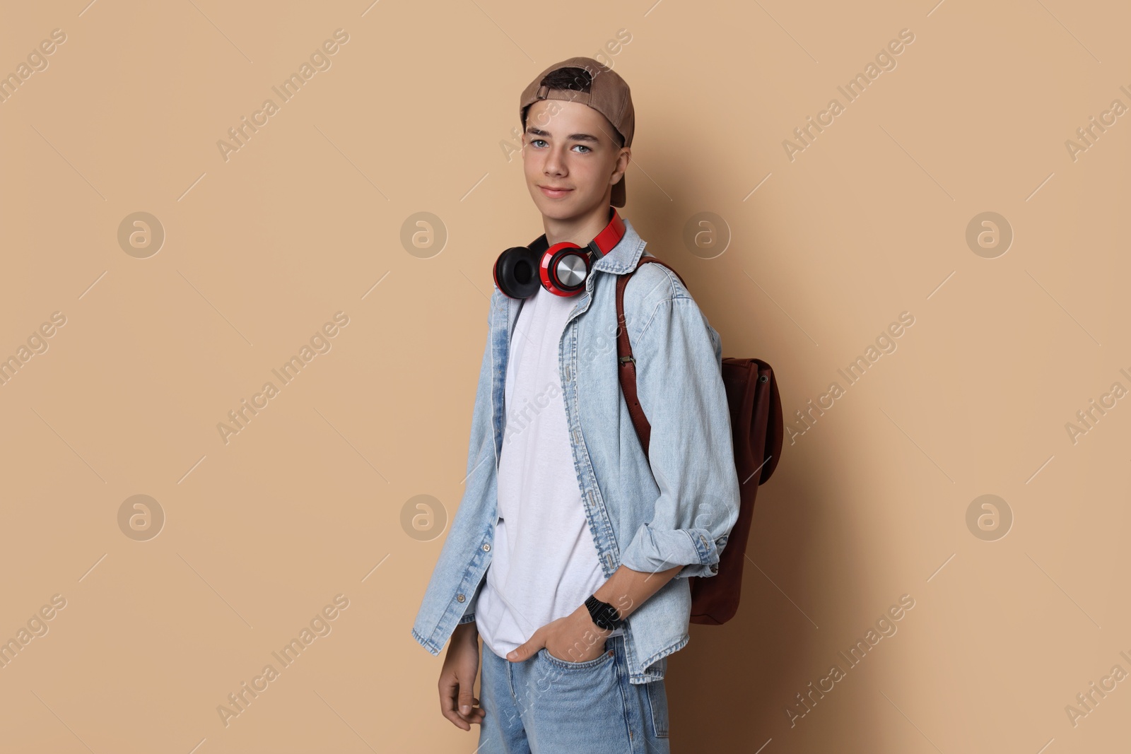 Photo of Portrait of teenage boy with backpack on dark beige background