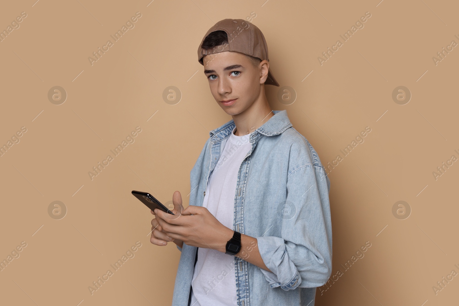 Photo of Portrait of teenage boy with smartphone on dark beige background