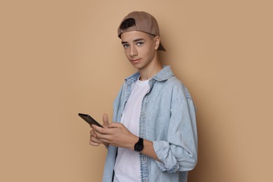 Portrait of teenage boy with smartphone on dark beige background