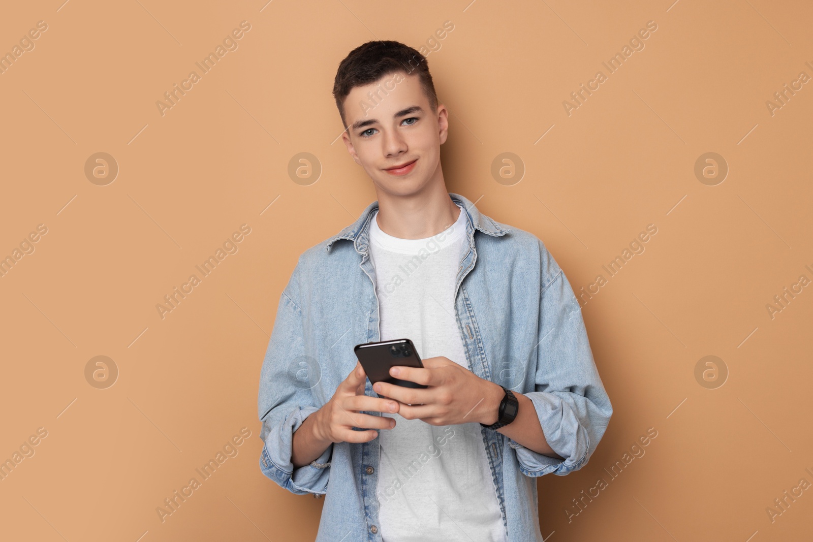 Photo of Portrait of teenage boy with smartphone on dark beige background