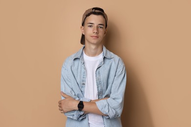 Photo of Portrait of teenage boy with crossed arms on dark beige background