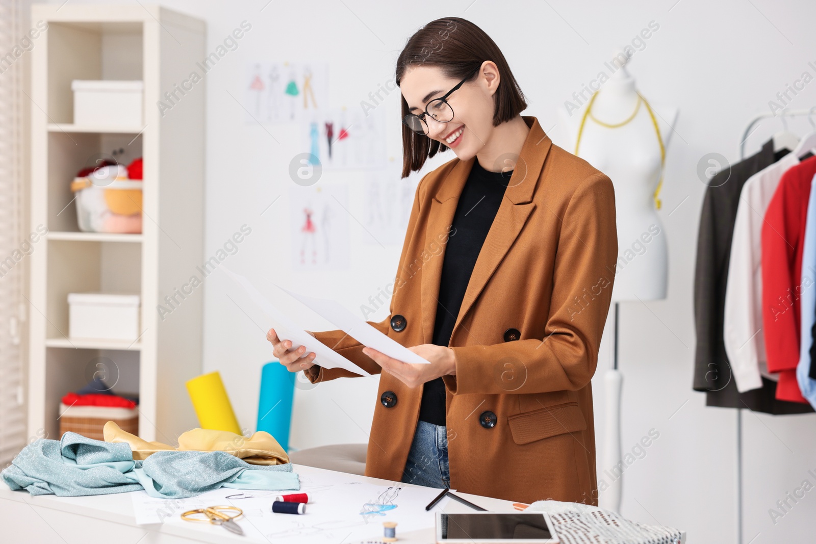 Photo of Fashion designer with sketches at table in workshop