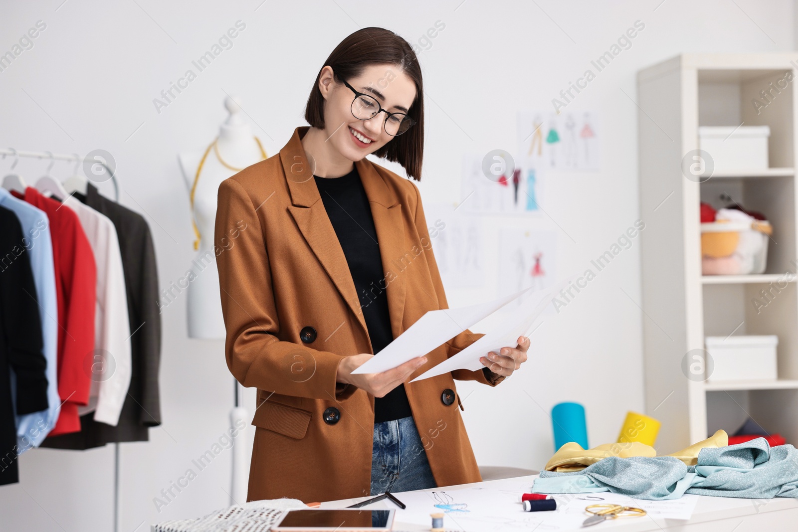 Photo of Fashion designer with sketches at table in workshop