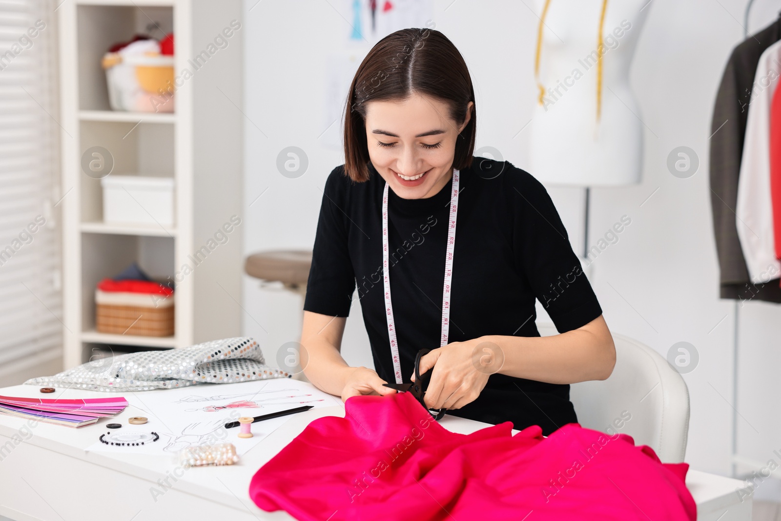 Photo of Fashion designer cutting pink fabric at table in workshop