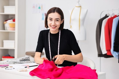 Photo of Fashion designer cutting pink fabric at table in workshop