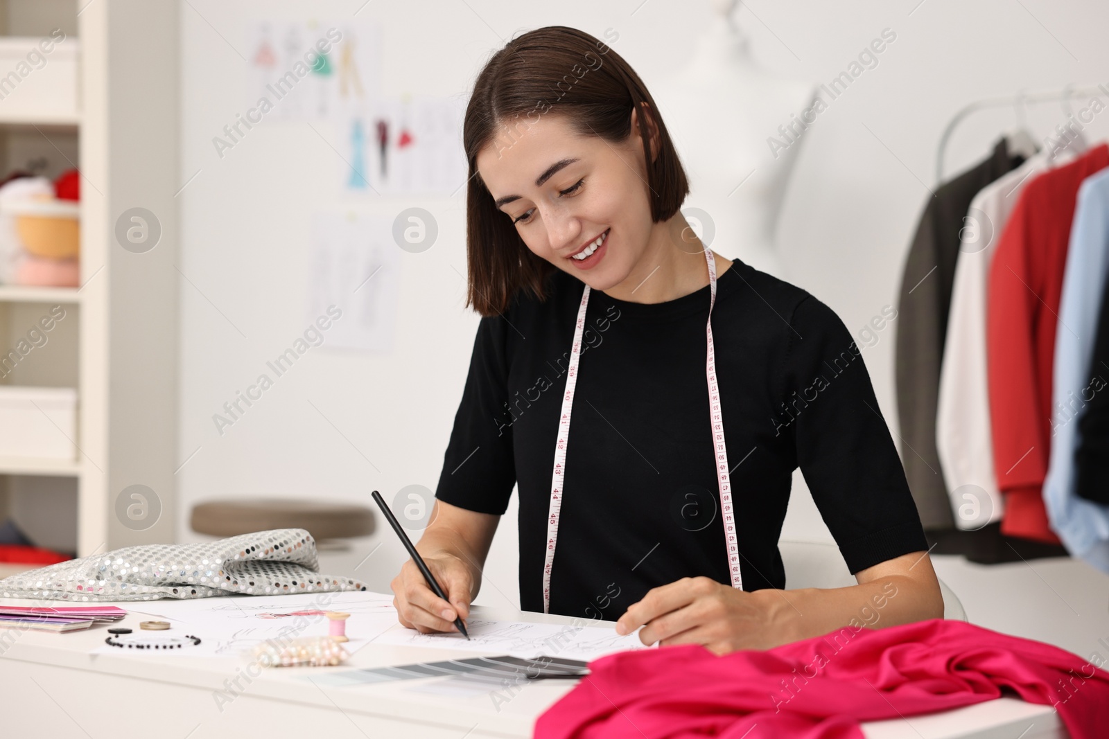 Photo of Fashion designer drawing sketch of beautiful outfit at table in workshop