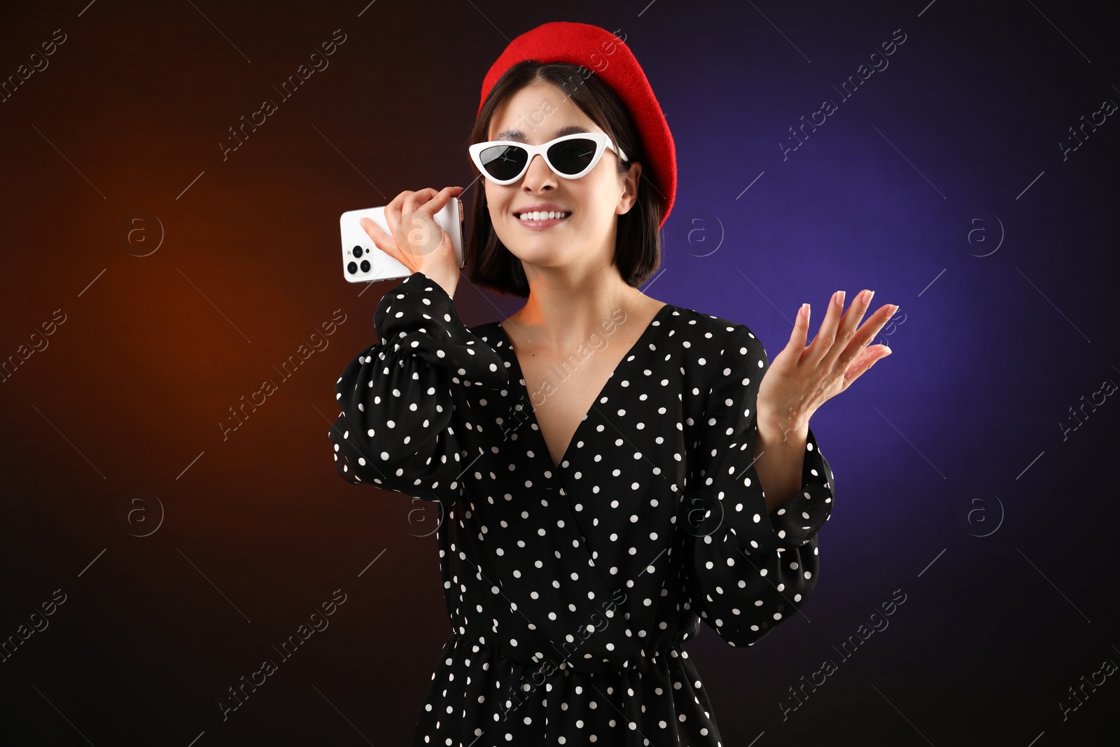 Photo of Stylish woman listening to voice message via smartphone on color background