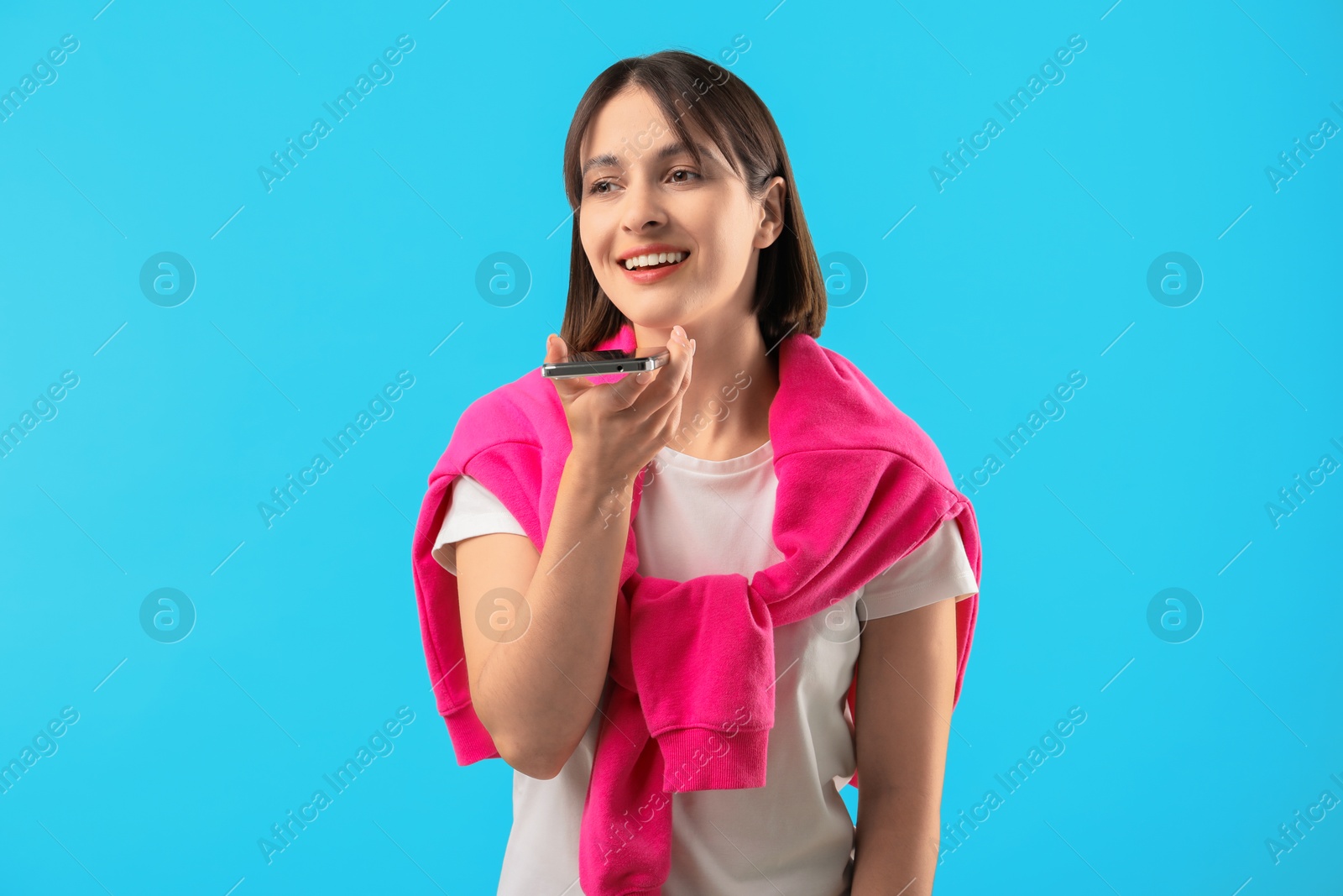 Photo of Beautiful woman recording voice message via smartphone on light blue background