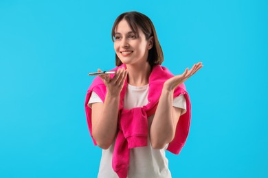 Beautiful woman recording voice message via smartphone on light blue background