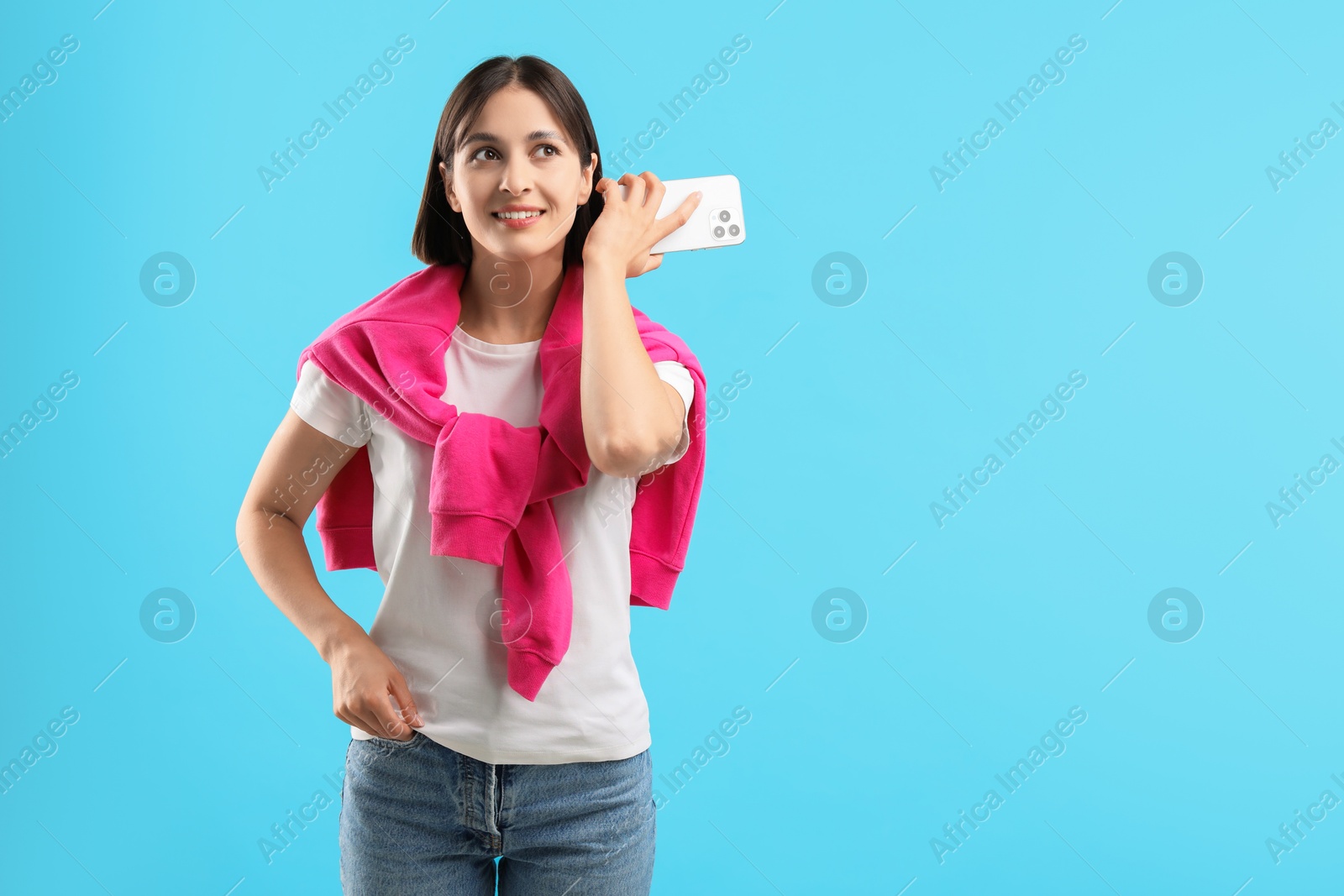 Photo of Beautiful woman with smartphone listening to voice message on light blue background, space for text