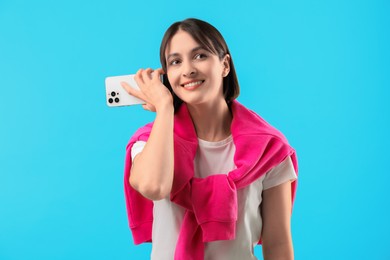 Photo of Beautiful woman with smartphone listening to voice message on light blue background