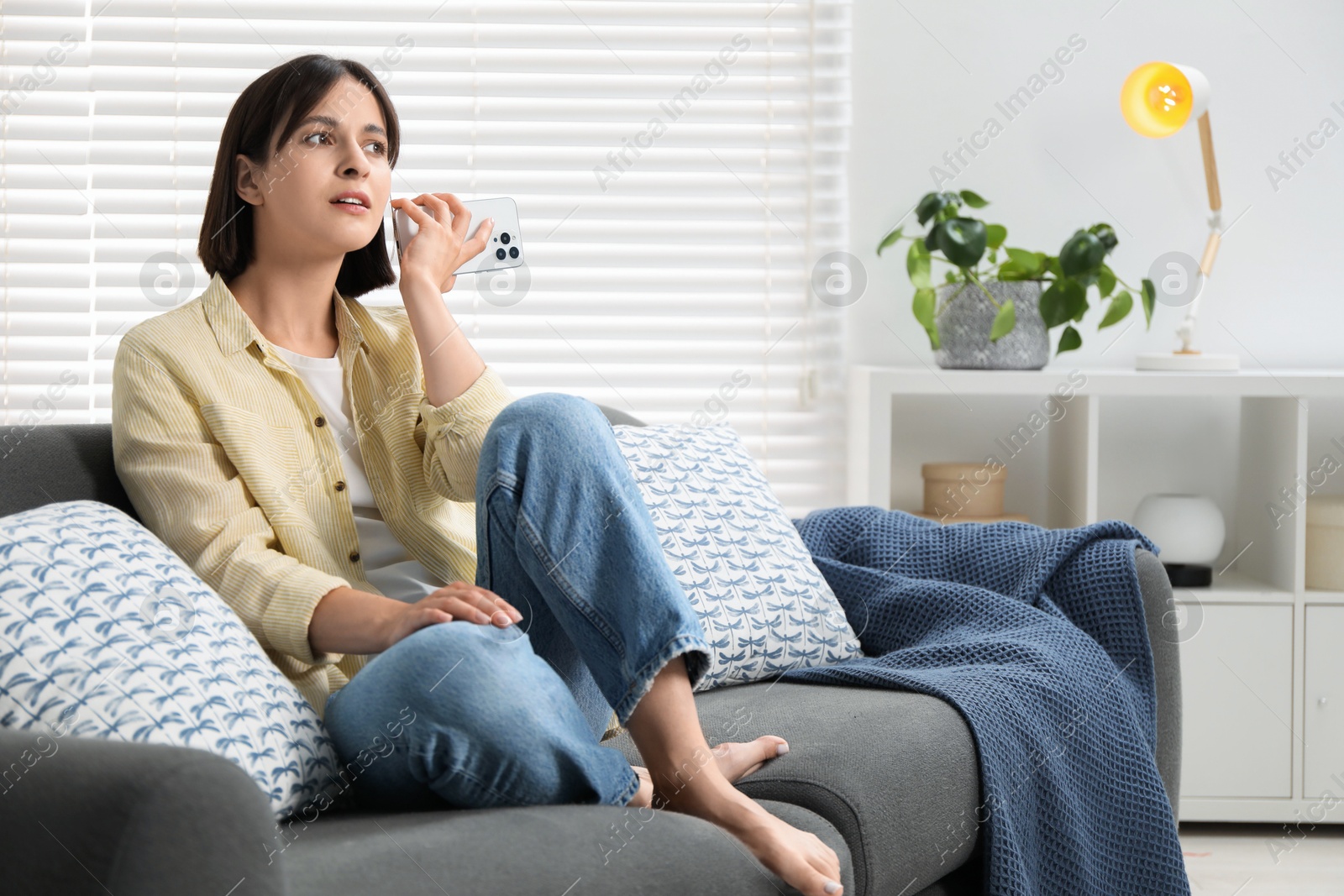 Photo of Beautiful woman with smartphone listening to voice message at home