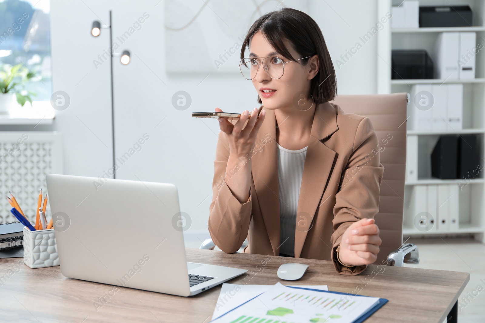 Photo of Beautiful woman recording voice message via smartphone in office