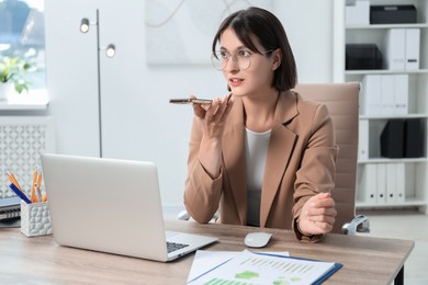 Beautiful woman recording voice message via smartphone in office